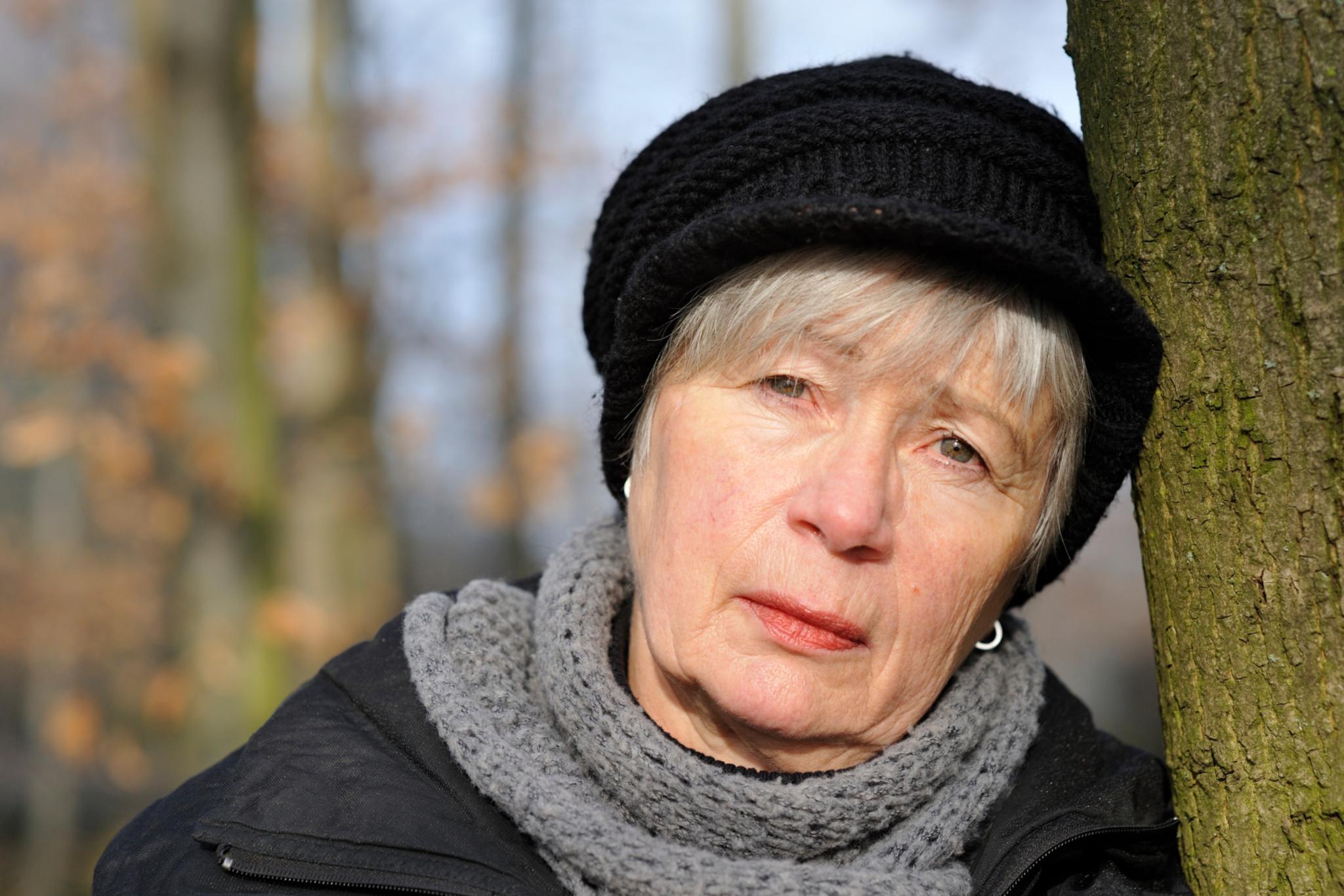 Eine Frau mit Schal und Mütze lehnt an einem Baumstamm